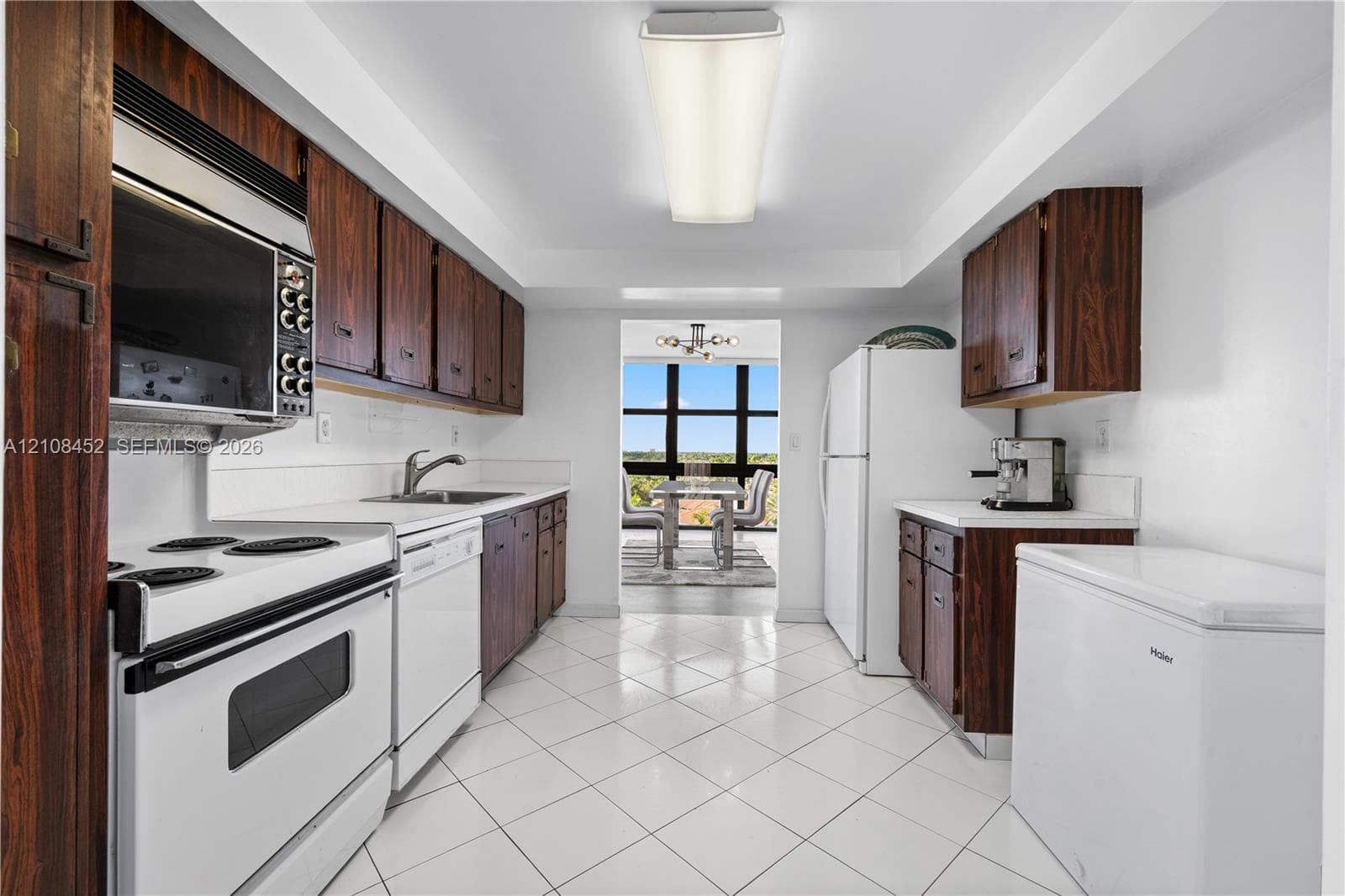 Kitchen featuring wood-finish cabinetry, white tile flooring, integrated white appliances, and a rectangular ceiling-mounted light fixture