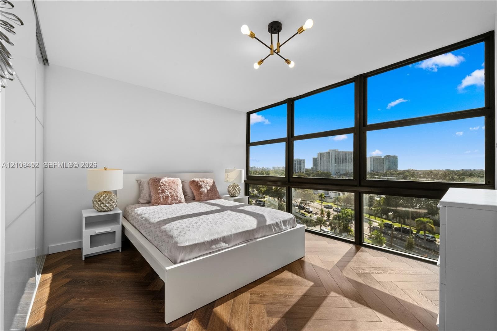 Floor-to-ceiling windows, chevron-patterned wood-finish flooring, built-in panel-front wardrobe, and a multi-arm geometric ceiling fixture