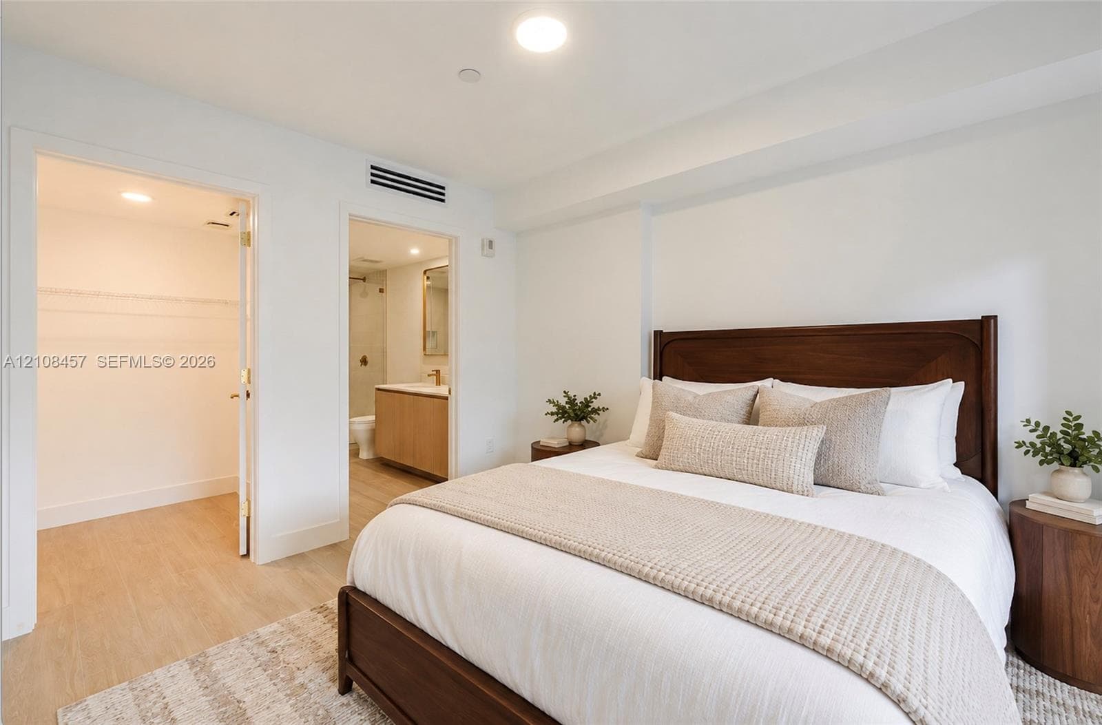 Neutral-toned wood-finish flooring, walk-in closet with built-in shelving, and bathroom featuring a light-finish wood vanity with a solid-surface countertop