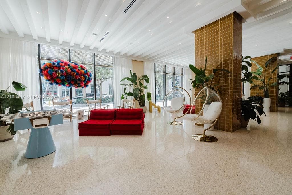 Spacious common area featuring floor-to-ceiling glass windows, recessed ceiling lighting, light-toned stone-finish flooring, and a structural column with mustard-colored tile cladding