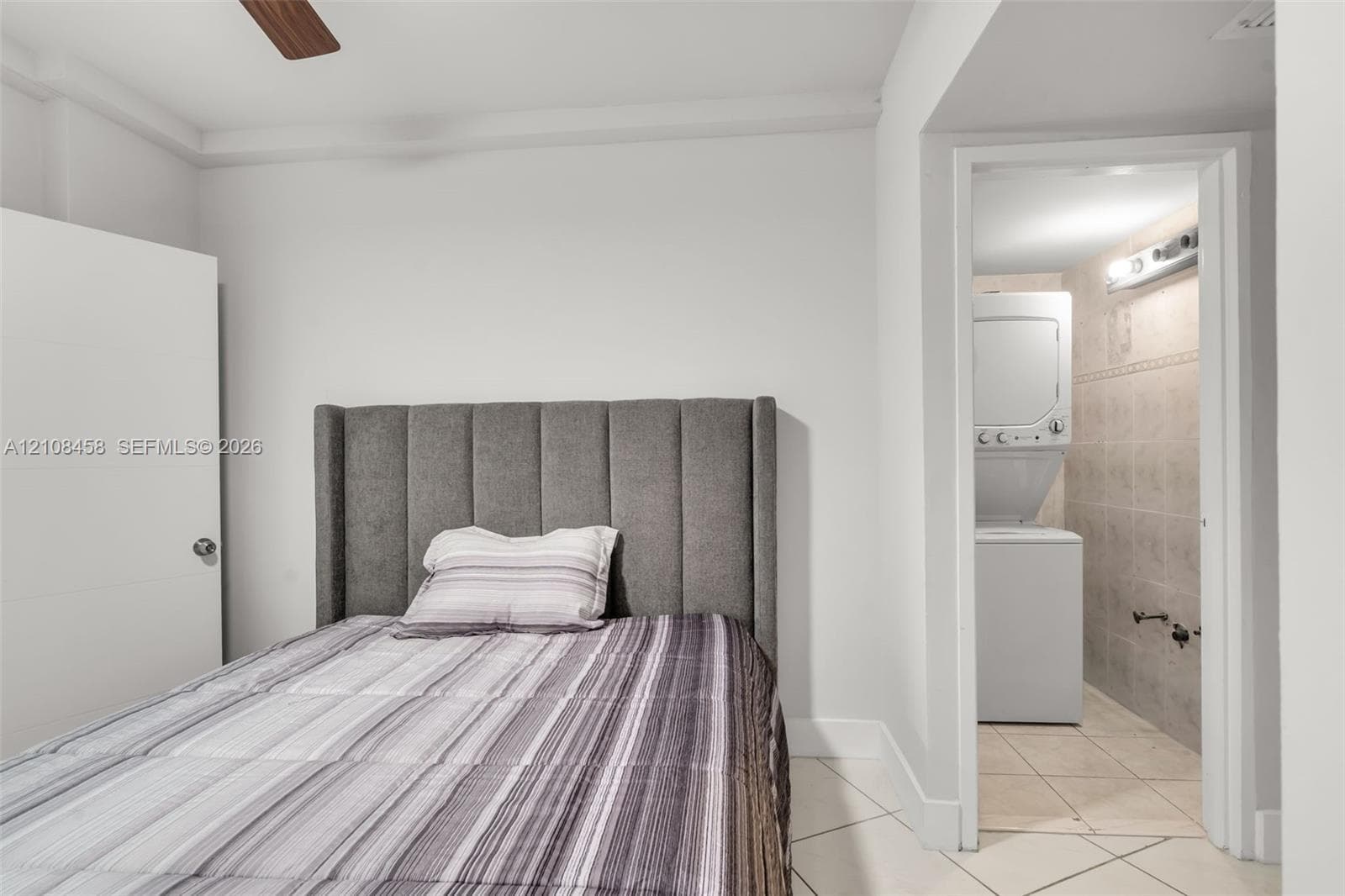 Interior space featuring white walls, tiled flooring, ceiling fan, and a dedicated laundry area with stacked washer and dryer unit