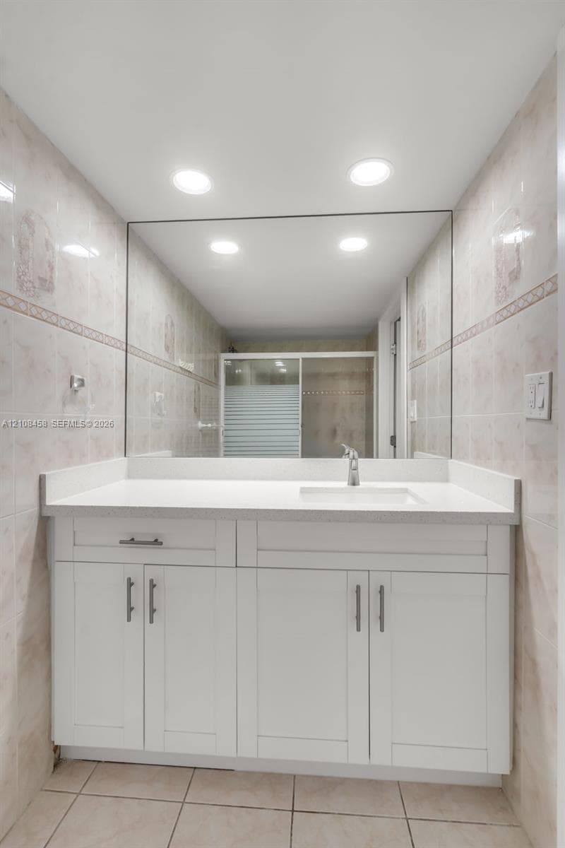 White shaker-style cabinetry vanity with a solid surface countertop, integrated sink, large frameless mirror, and recessed lighting