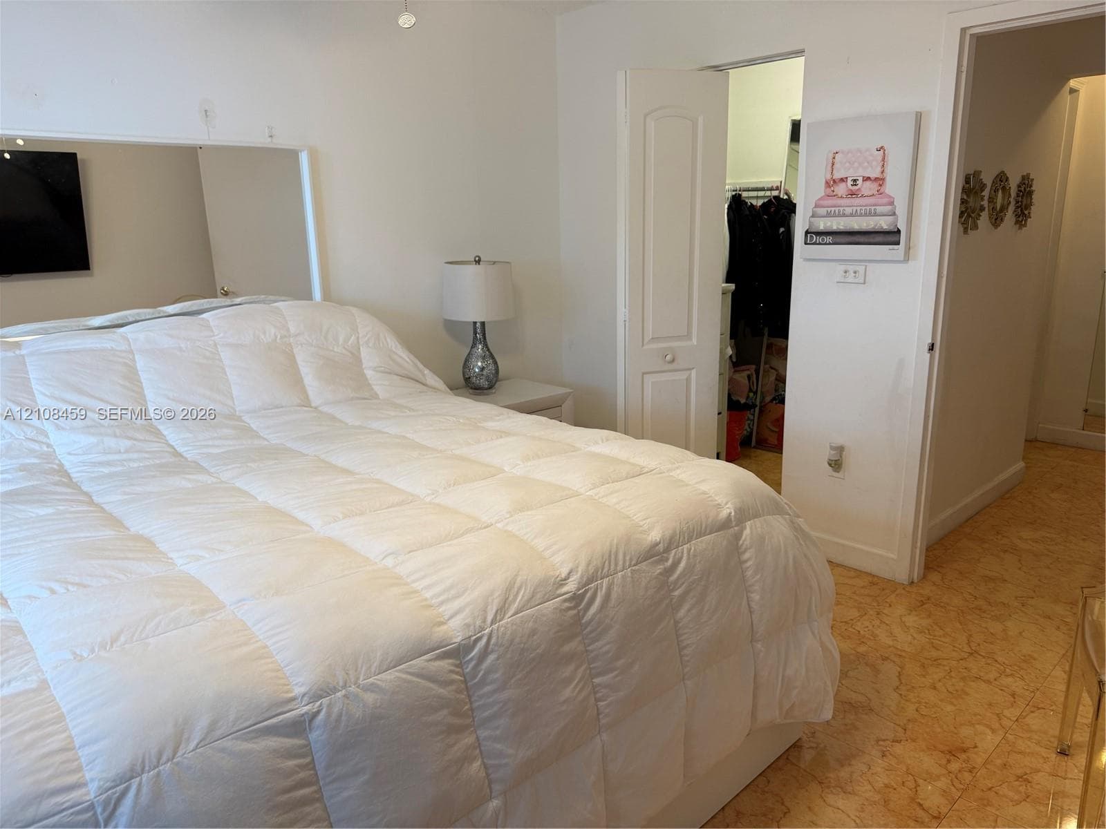 Bedroom featuring a large wall-mounted mirror, neutral interior paint, stone-finish tile flooring, and a walk-in closet with an arched two-panel door