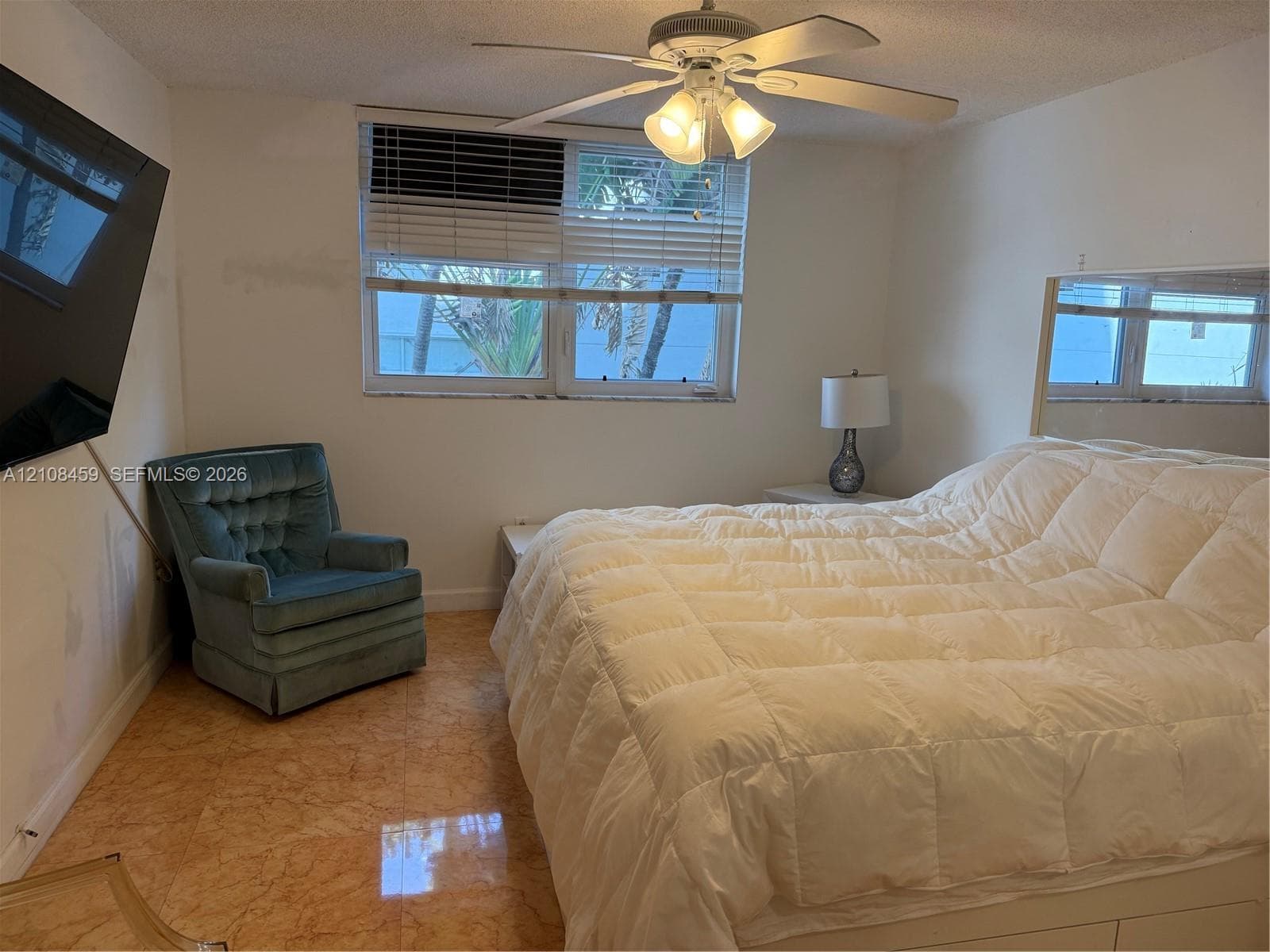 Polished stone flooring, ceiling-mounted fan with integrated light fixture, large-format wall mirror, and window with blinds
