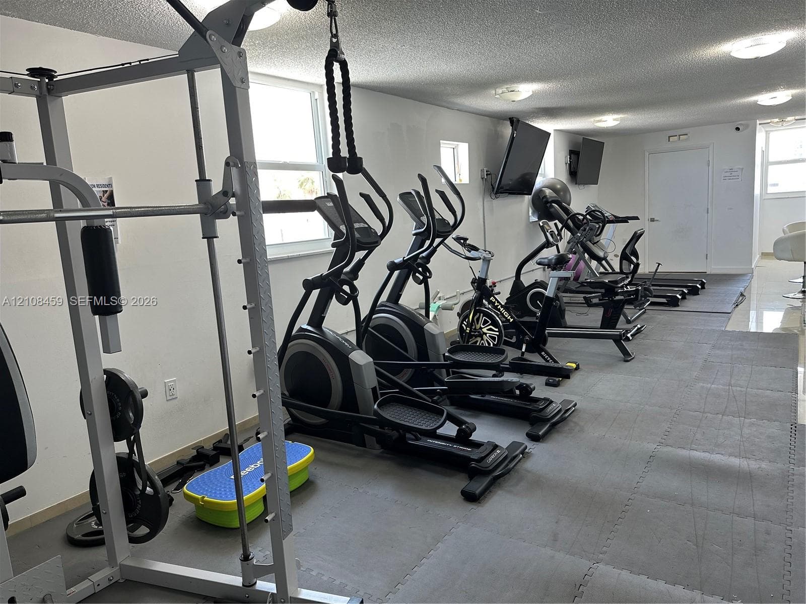 Fitness area featuring tile flooring, ceiling-mounted lighting, and wall-mounted televisions