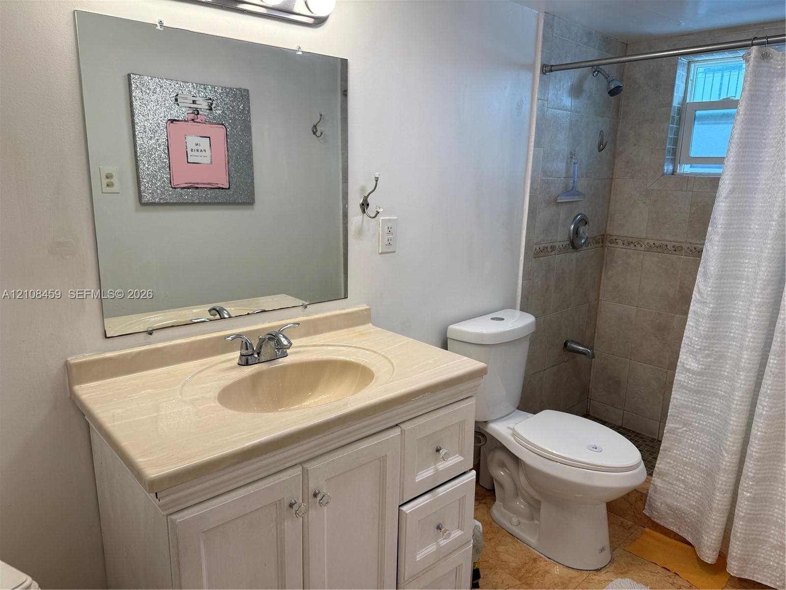 Vanity with stone-finish countertop, integrated sink, and white cabinetry, paired with a square wall-mounted mirror, ceramic tile shower surround, and chrome shower fixtures