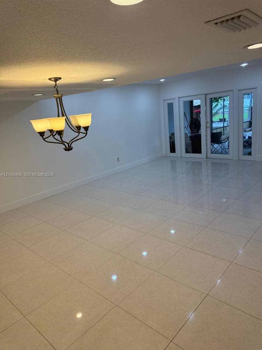 Large-format tile flooring, recessed ceiling lighting, and a multi-arm chandelier with glass shades, featuring double glass-paneled exterior doors with flanking sidelights