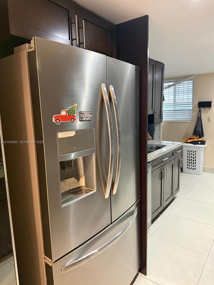Stainless steel French-door refrigerator, dark-finish cabinetry with silver-tone hardware, stone-composite countertops, and tile flooring