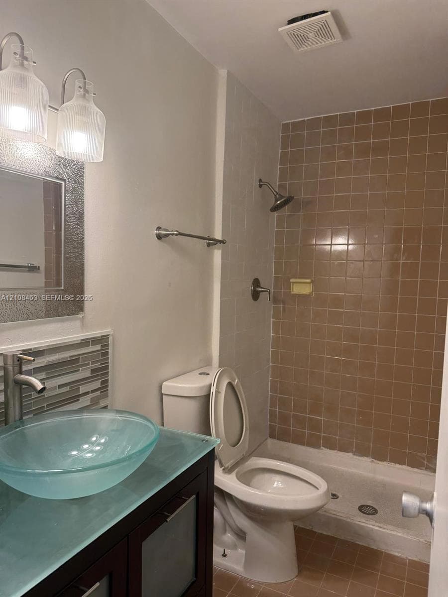 Bathroom featuring a dark wood-finish vanity, glass vessel sink, mosaic tile backsplash, and a tub-shower combination with ceramic wall tile
