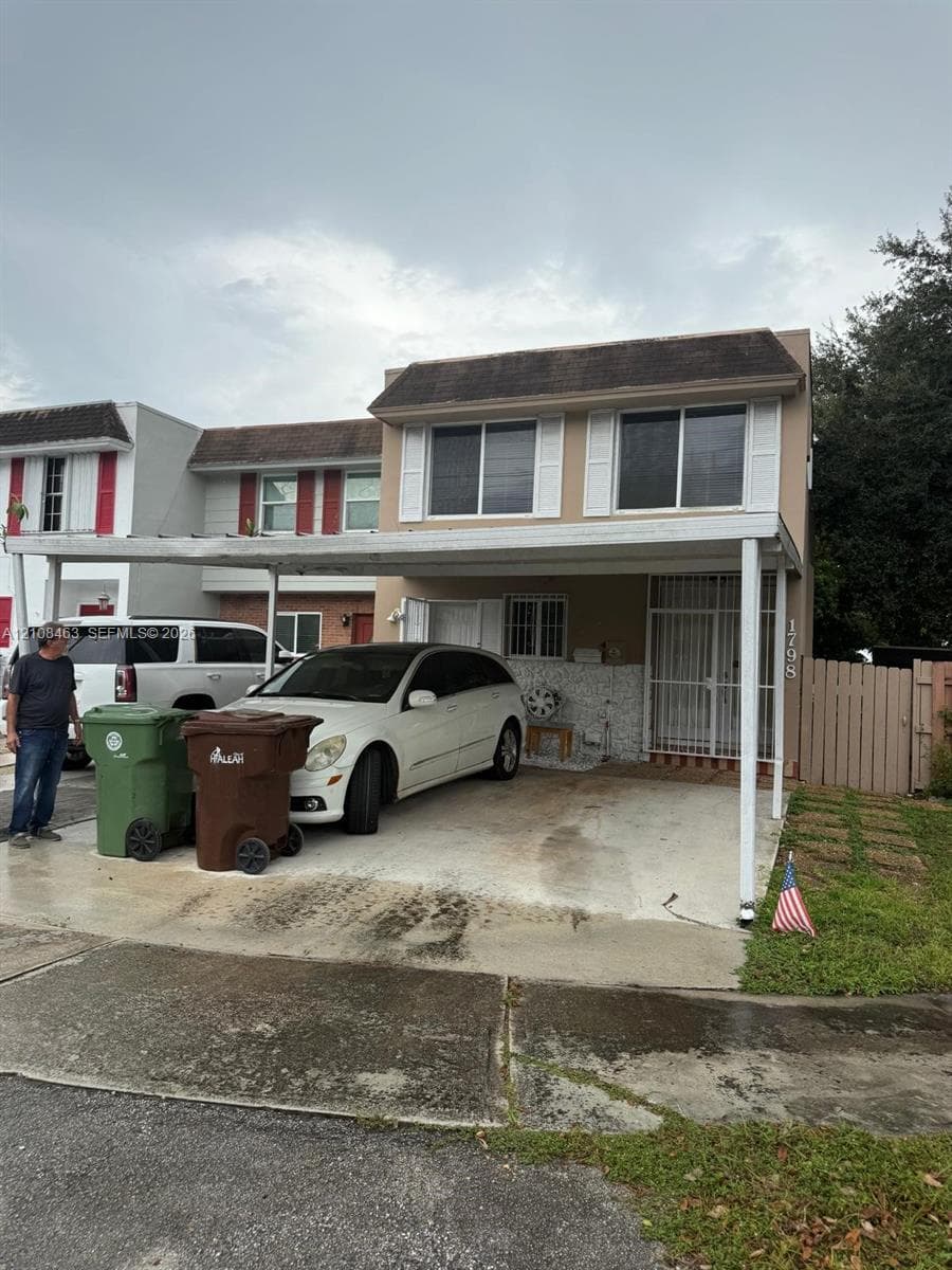 Two-story residence featuring a concrete driveway, attached metal carport, exterior shutters, and a security-style entry screen door