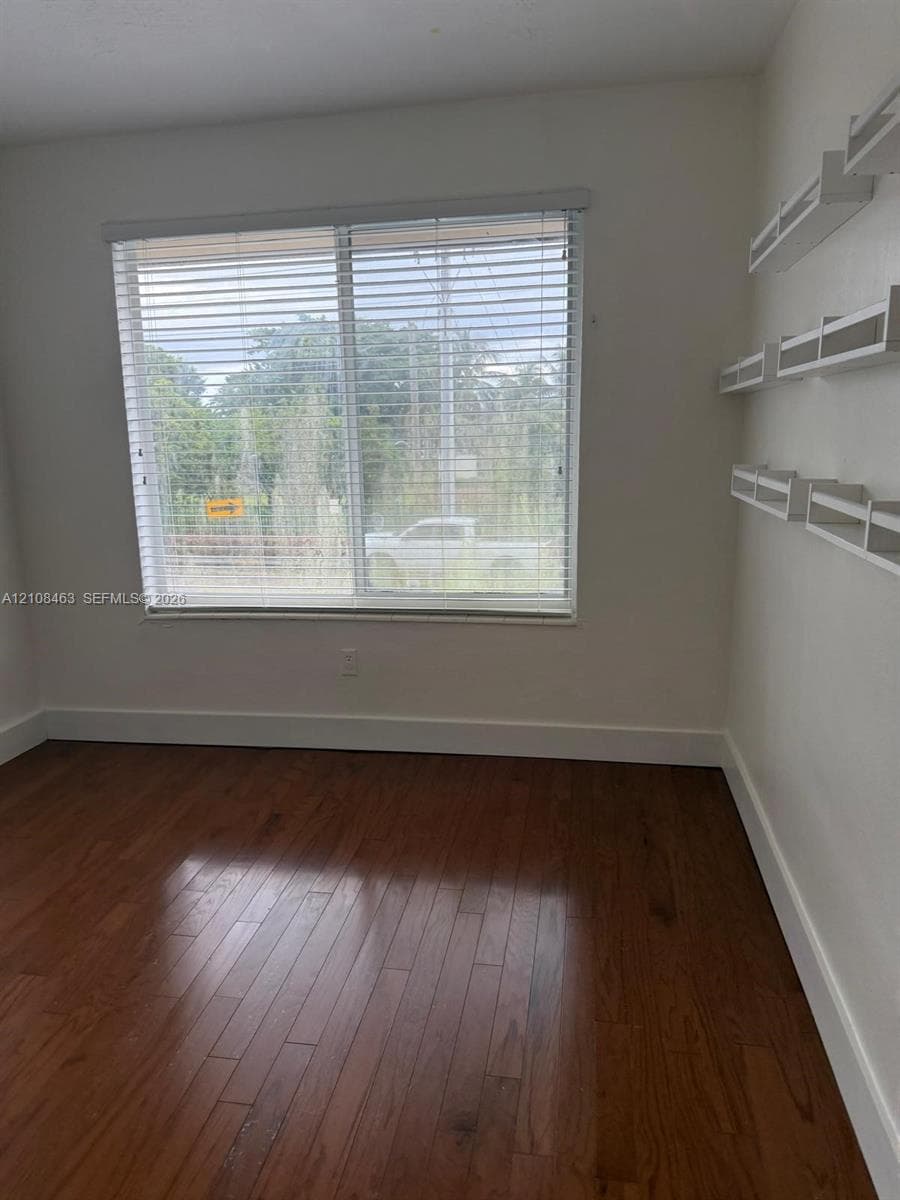 Room featuring wood-finish flooring, a large window with horizontal blinds, and white built-in wall shelving