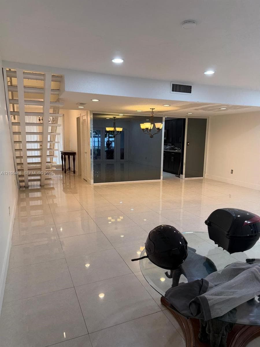 Large-format tile flooring, open staircase with white-finish metal railings, recessed ceiling lighting, and mirrored wall accents