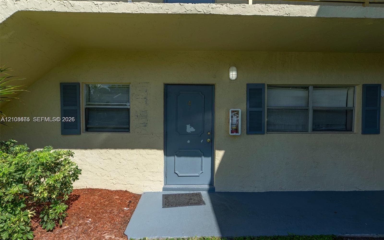 Exterior entry featuring a textured facade, blue-painted door, dark-toned shutters, and a concrete landing