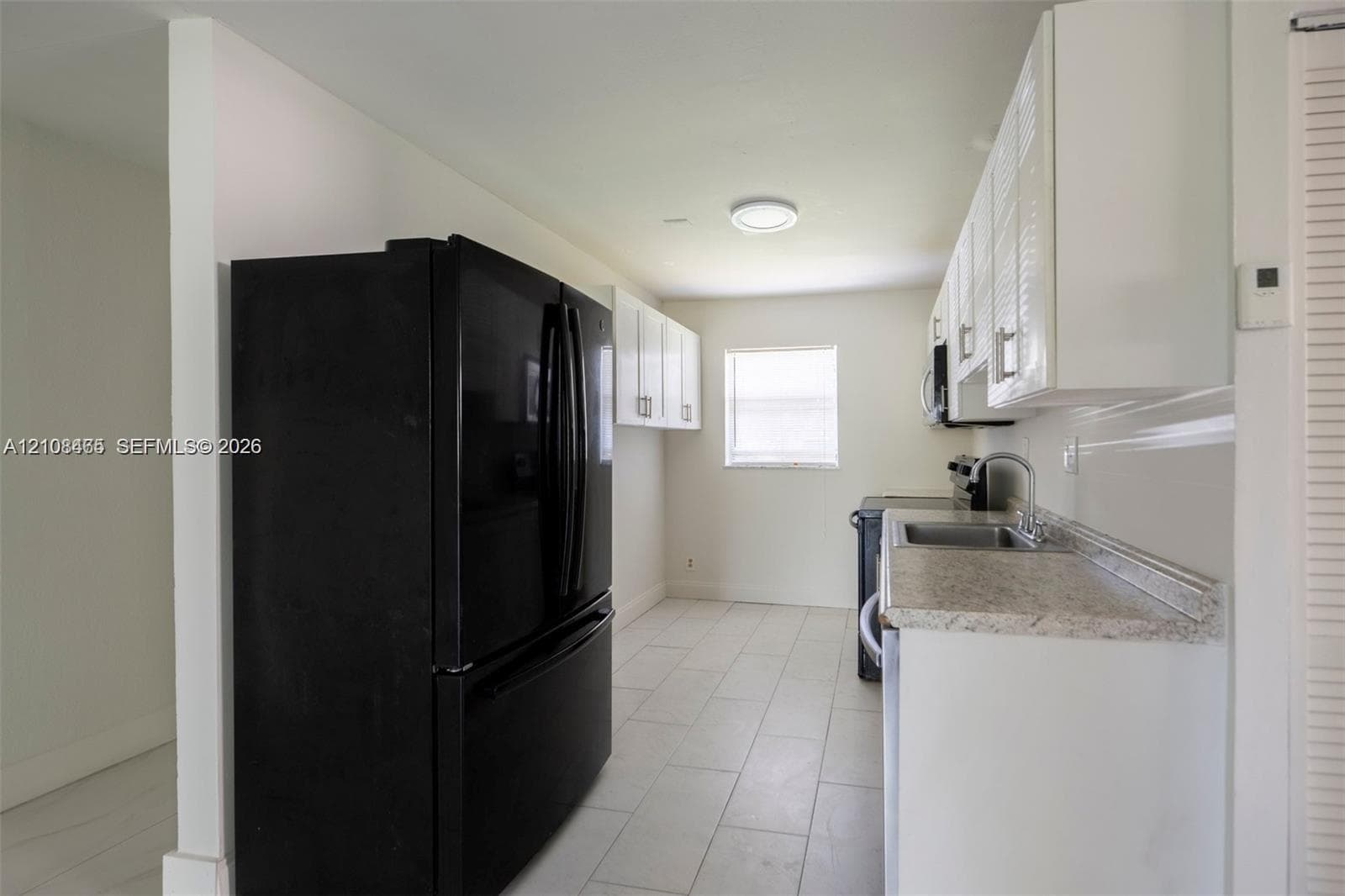 Kitchen featuring white shaker-style cabinetry, stone-finish countertops, tile flooring, and integrated black appliances