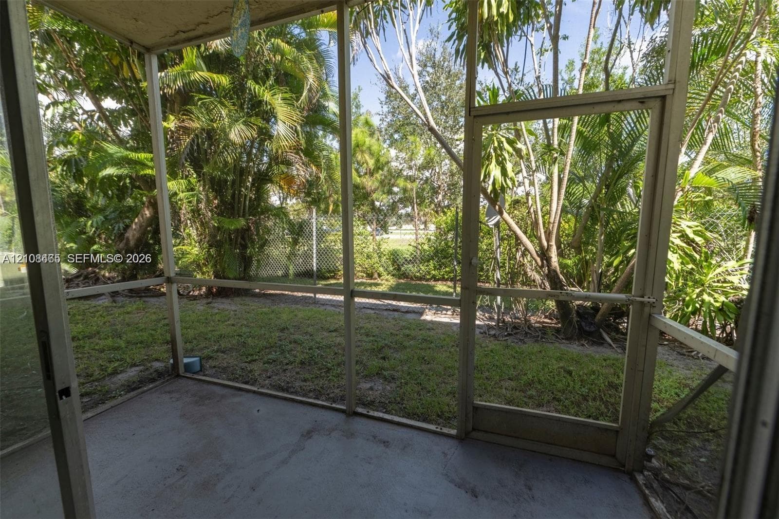 Screened-in patio with a concrete floor, metal framing, and direct access to a fenced yard featuring mature foliage
