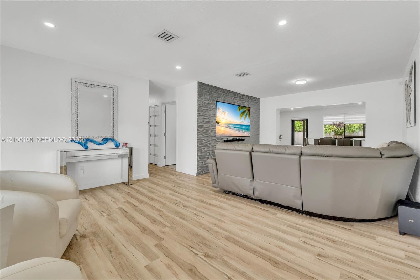 Living area featuring wood-finish flooring, recessed lighting, and a grey textured accent wall