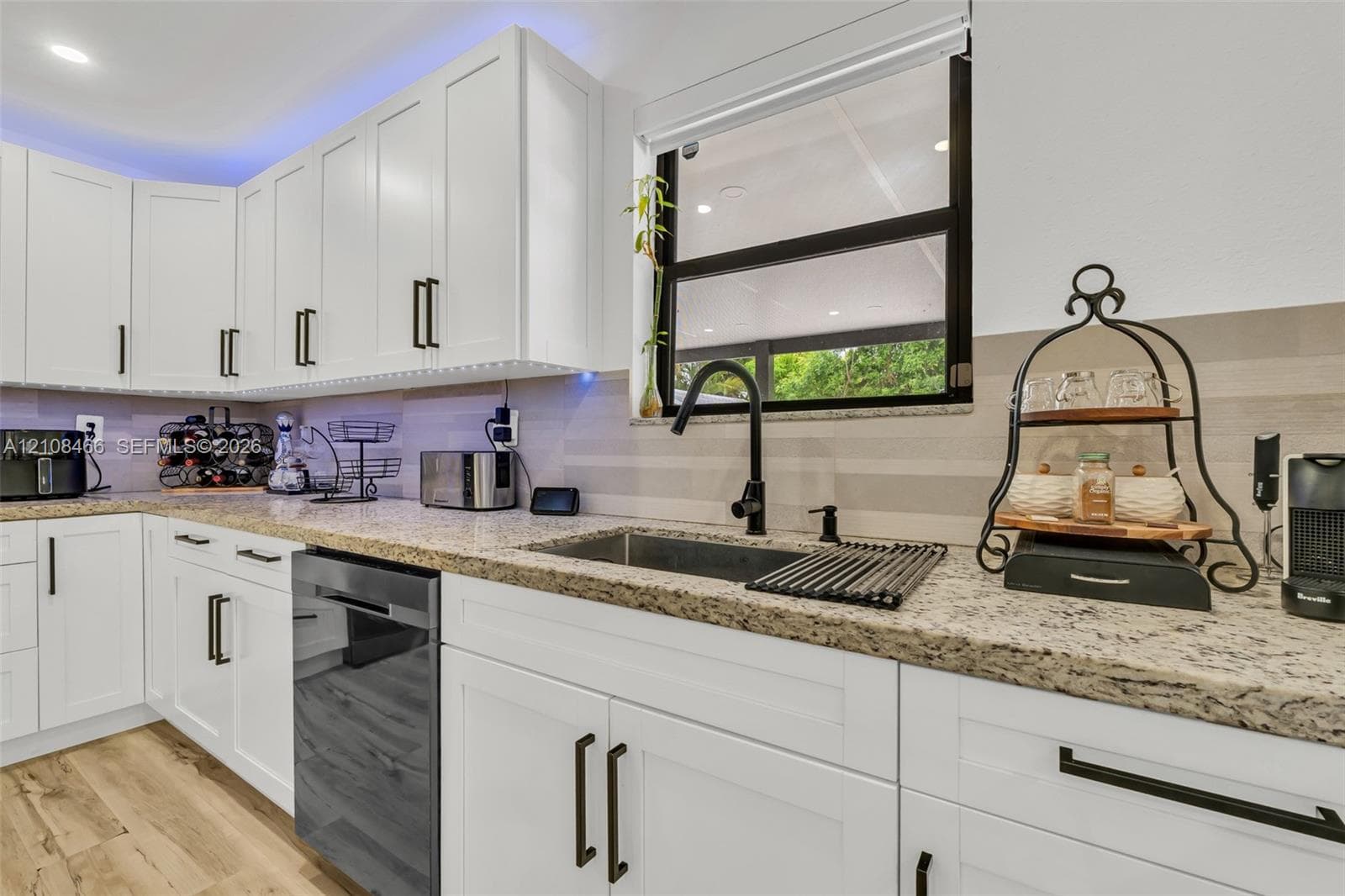 Kitchen featuring white shaker-style cabinetry, stone countertops, horizontal tile backsplash, wood-finish flooring, and a matte black gooseneck faucet