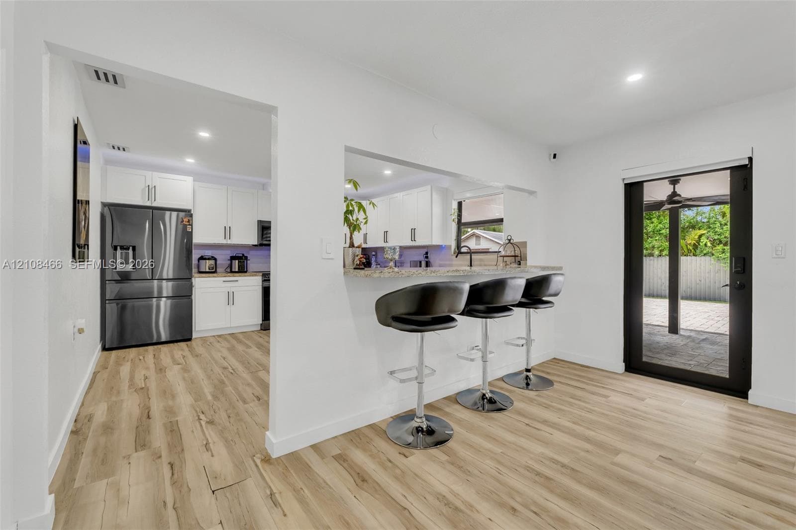 Kitchen featuring white shaker cabinetry, stone-finish countertops, stainless steel appliances, wood-finish flooring, and a breakfast bar cutout