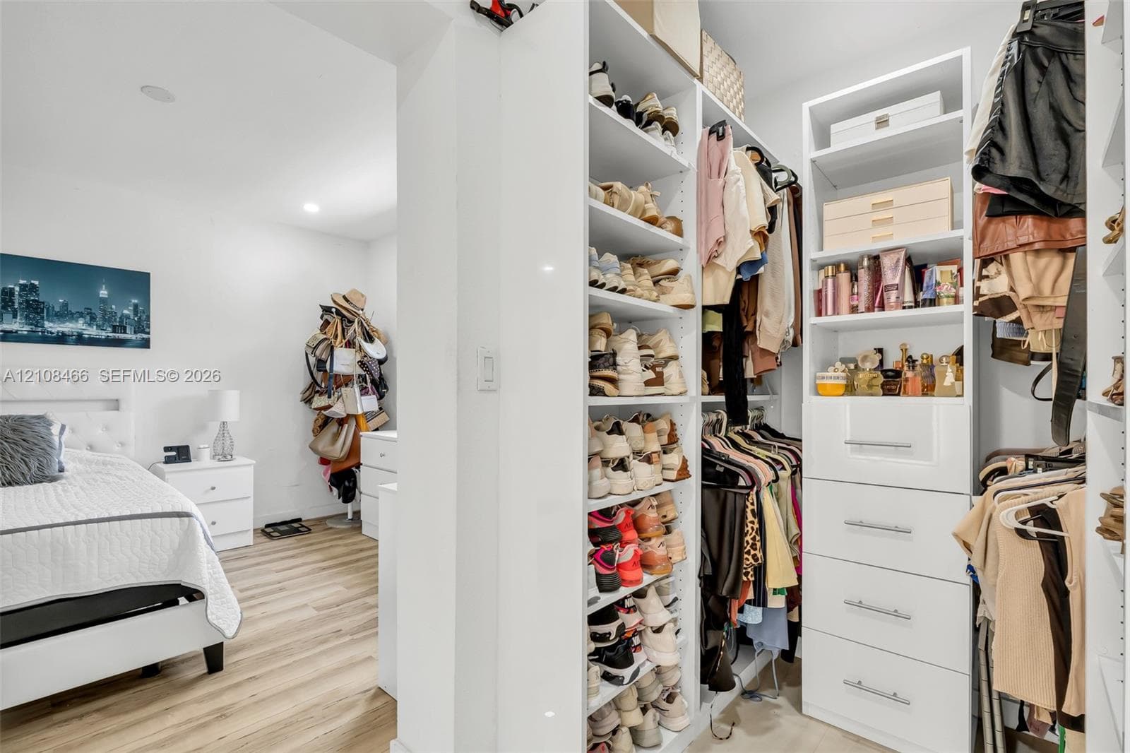 Custom walk-in closet featuring floor-to-ceiling white shelving, integrated cabinetry with four drawers, and recessed lighting