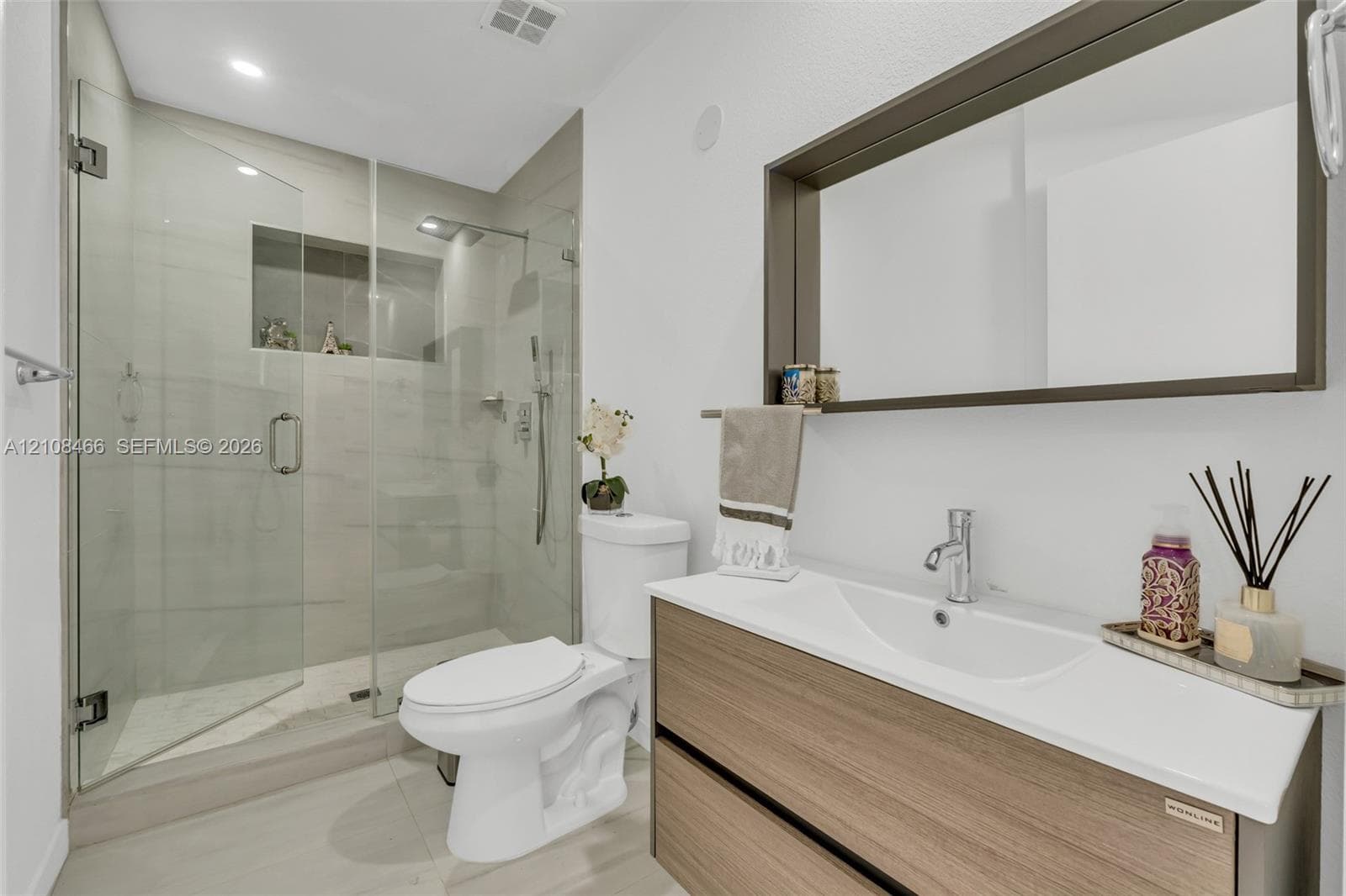Floating wood-finish vanity with an integrated sink, frameless glass walk-in shower featuring a tiled inset niche, and a wall-mounted framed mirror