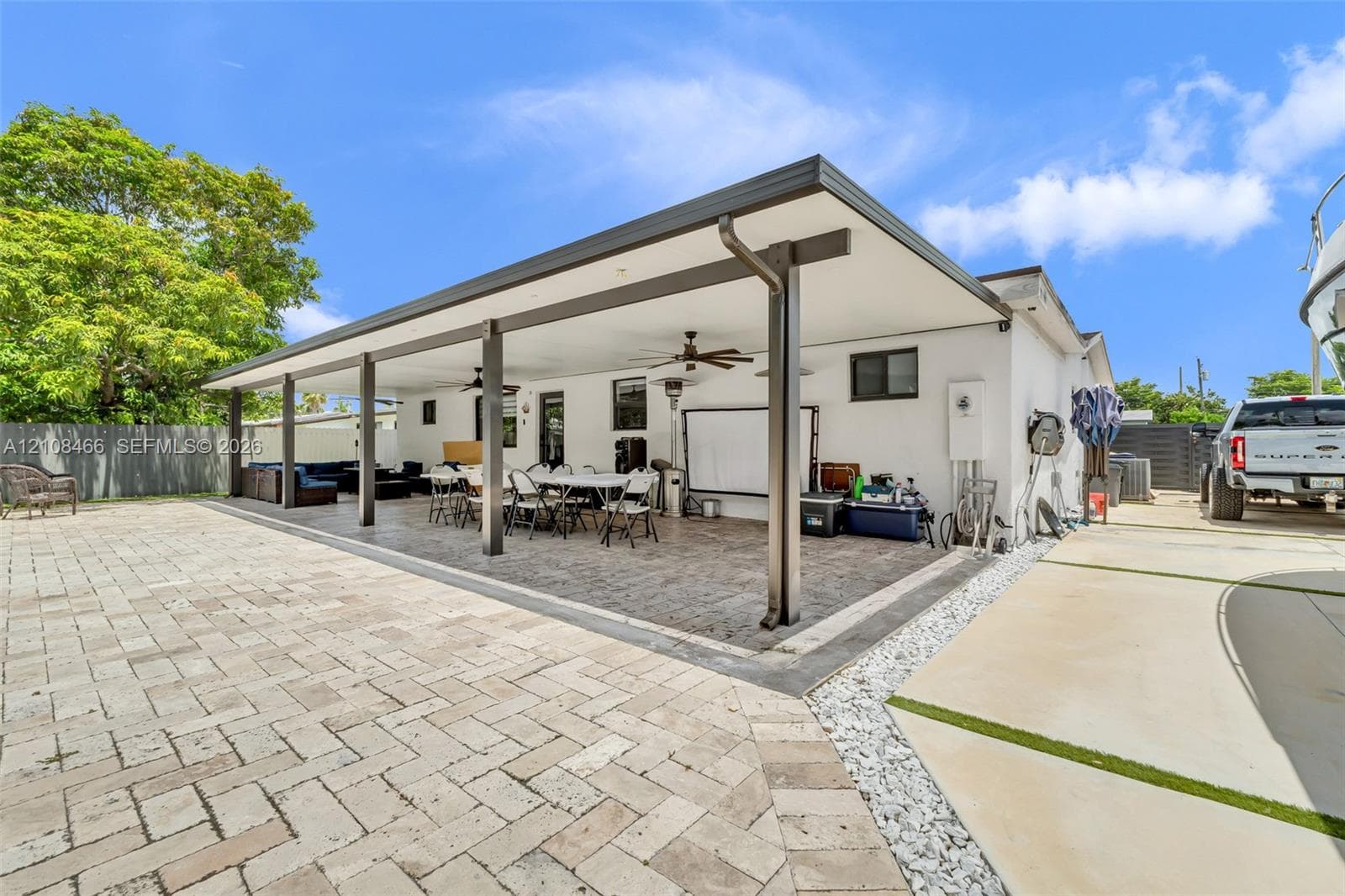 Covered patio featuring a stamped concrete floor, recessed lighting, and ceiling fans, complemented by a herringbone-patterned paver terrace and concrete driveway