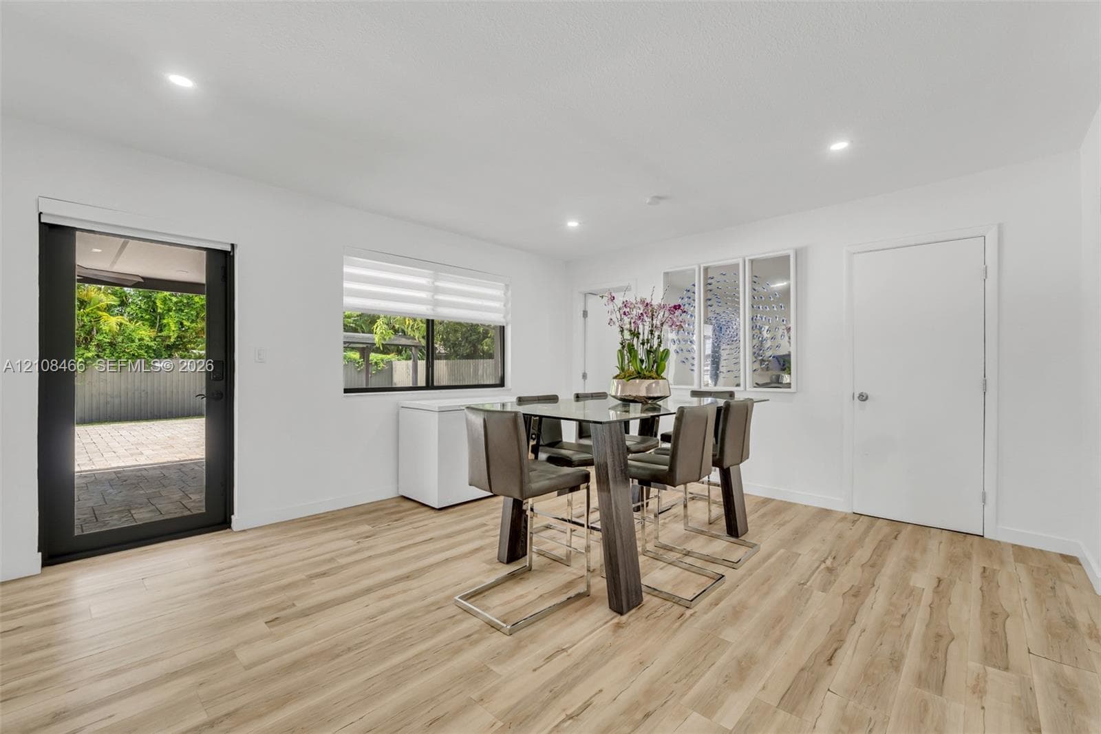 Wood-finish flooring, recessed lighting, neutral wall paint, window with roller shade, and exterior glass door with black frame