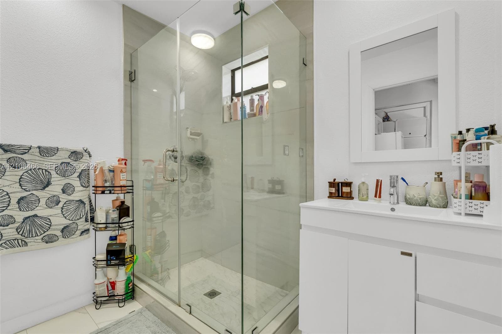 Frameless glass shower enclosure with tiled walls, white vanity featuring an integrated sink, and a wall-mounted framed mirror