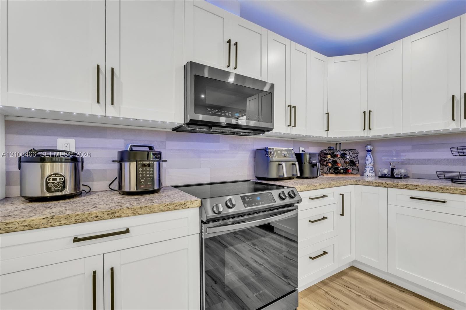 Kitchen featuring white shaker-style cabinetry, stone countertops, stainless steel appliances, and under-cabinet lighting