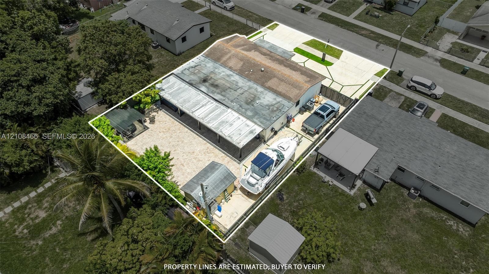 Aerial perspective of residential property featuring a concrete driveway, gated gravel parking area, metal-covered patio, and a detached storage structure