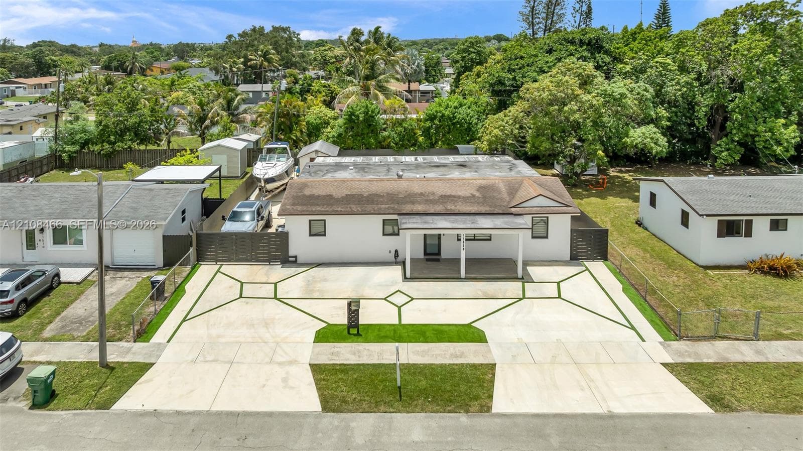 Expansive concrete driveway featuring geometric synthetic turf inlays, covered front porch, gated side storage area, and low-maintenance landscaping