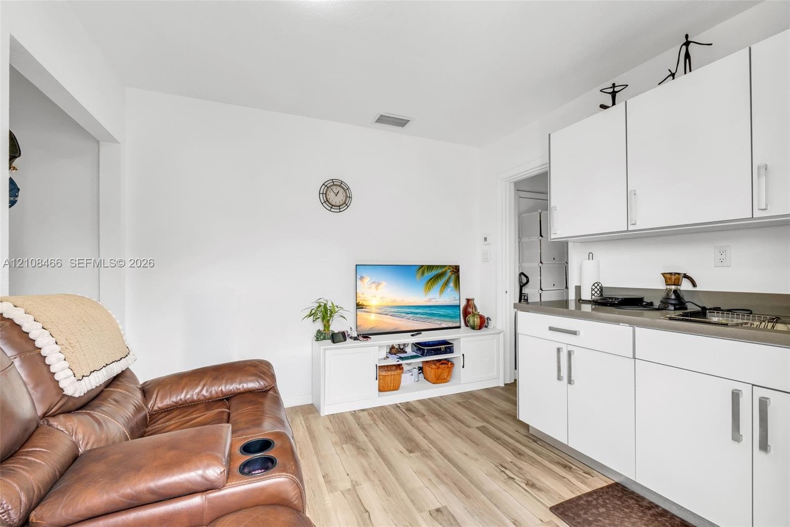 Kitchenette featuring white cabinetry with silver-tone hardware, solid-surface countertops, and wood-finish flooring
