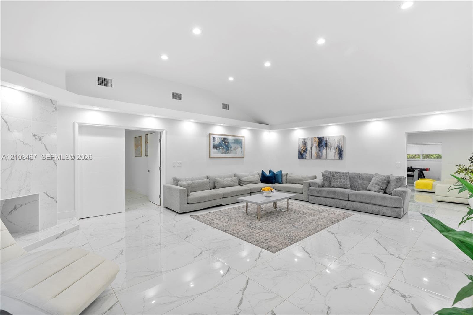 Open-concept interior featuring high vaulted ceilings, large-format tile flooring with a neutral finish, and a floor-to-ceiling stone-surround fireplace