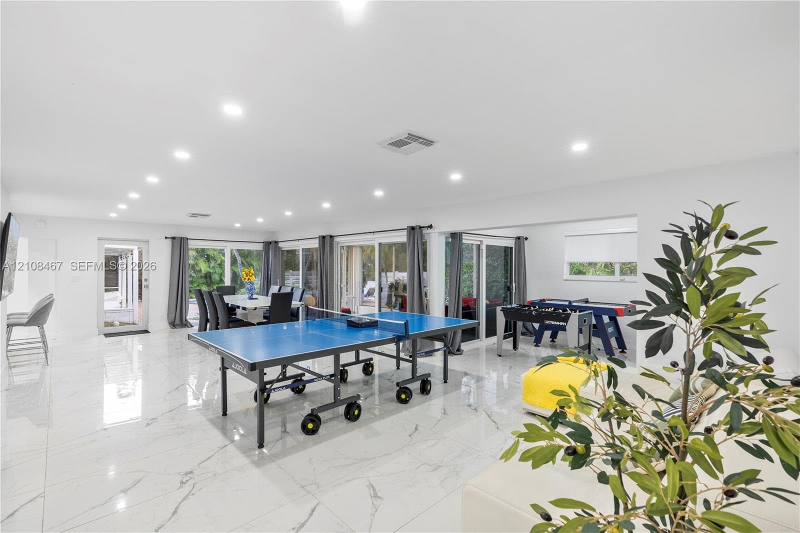 Open-concept interior featuring large-format tile flooring, recessed ceiling lighting, and multiple sliding glass doors providing access to the exterior
