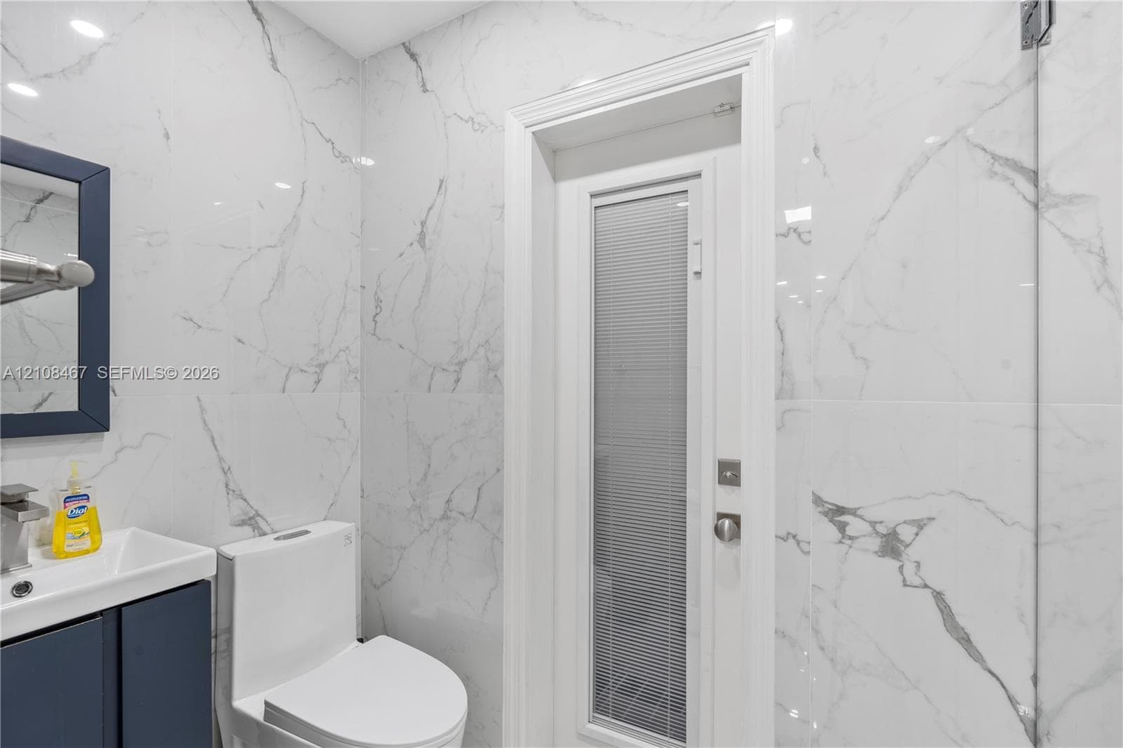 Full-height wall tiling with a veined pattern, vanity featuring a rectangular integrated sink, solid-color cabinetry, and a door with an integrated privacy glass pane