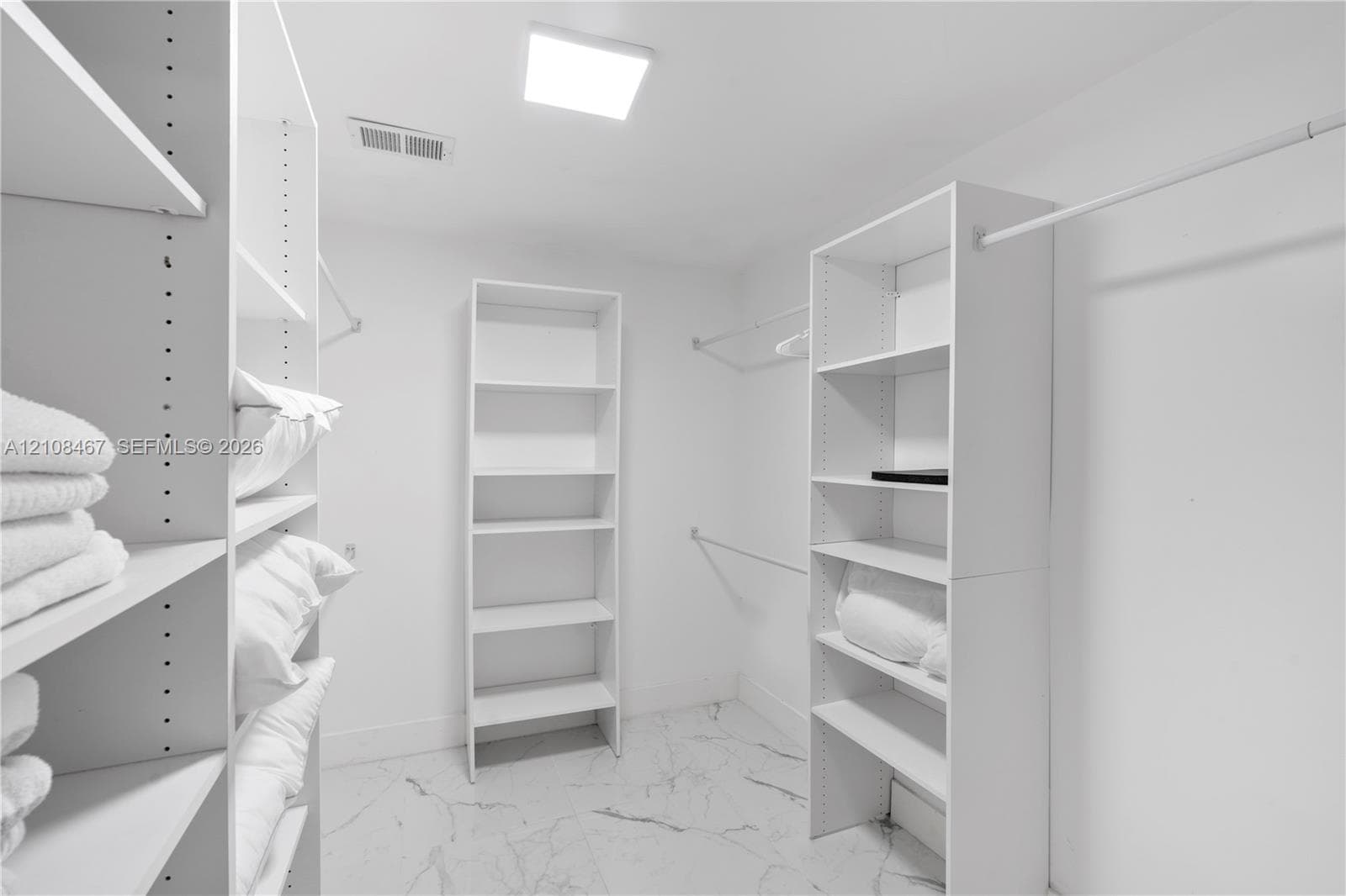 Walk-in closet featuring white built-in shelving, integrated hanging rods, and stone-finish flooring