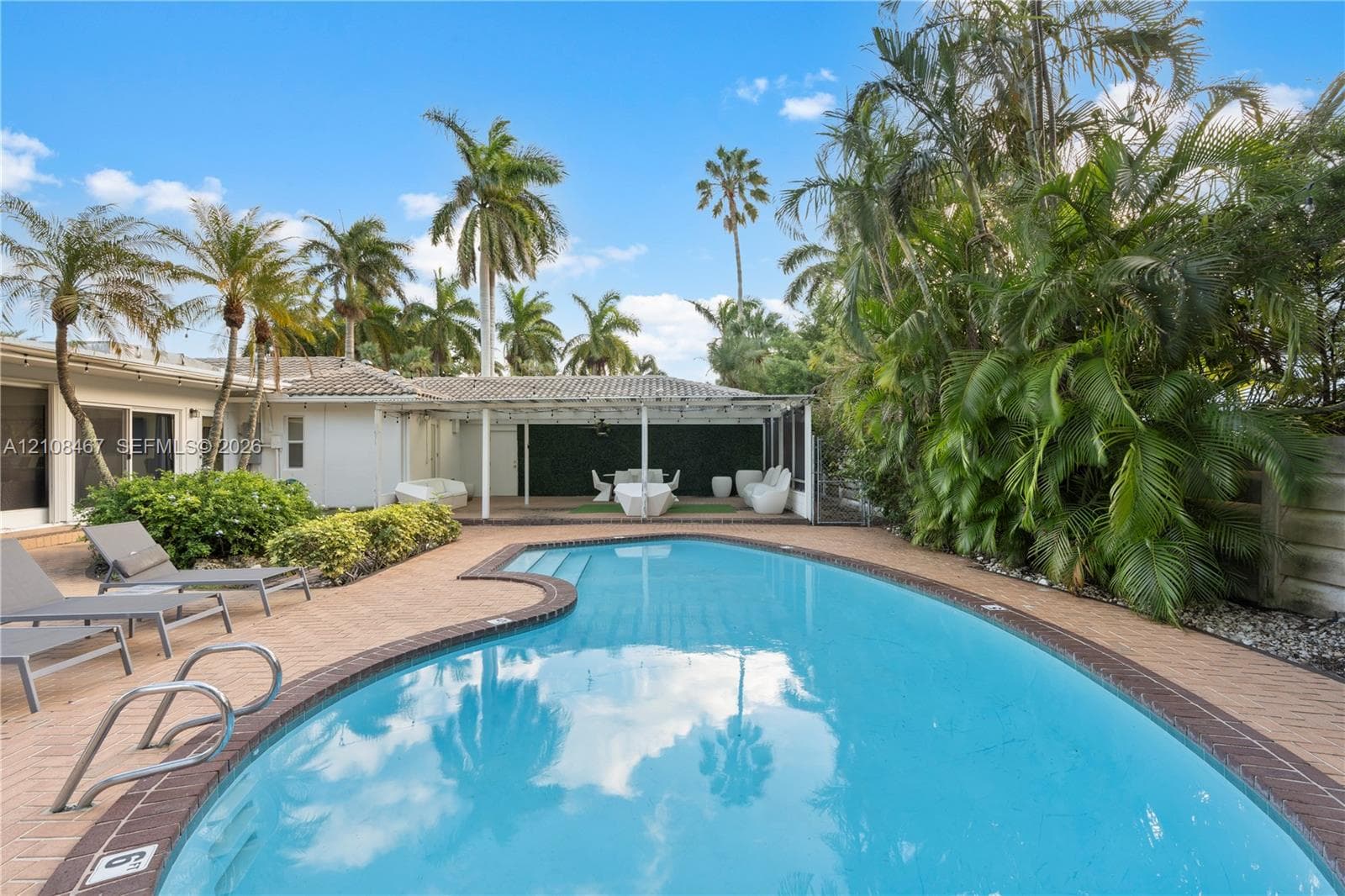 Custom-shaped swimming pool with tile surround, covered patio structure, and lush mature landscaping