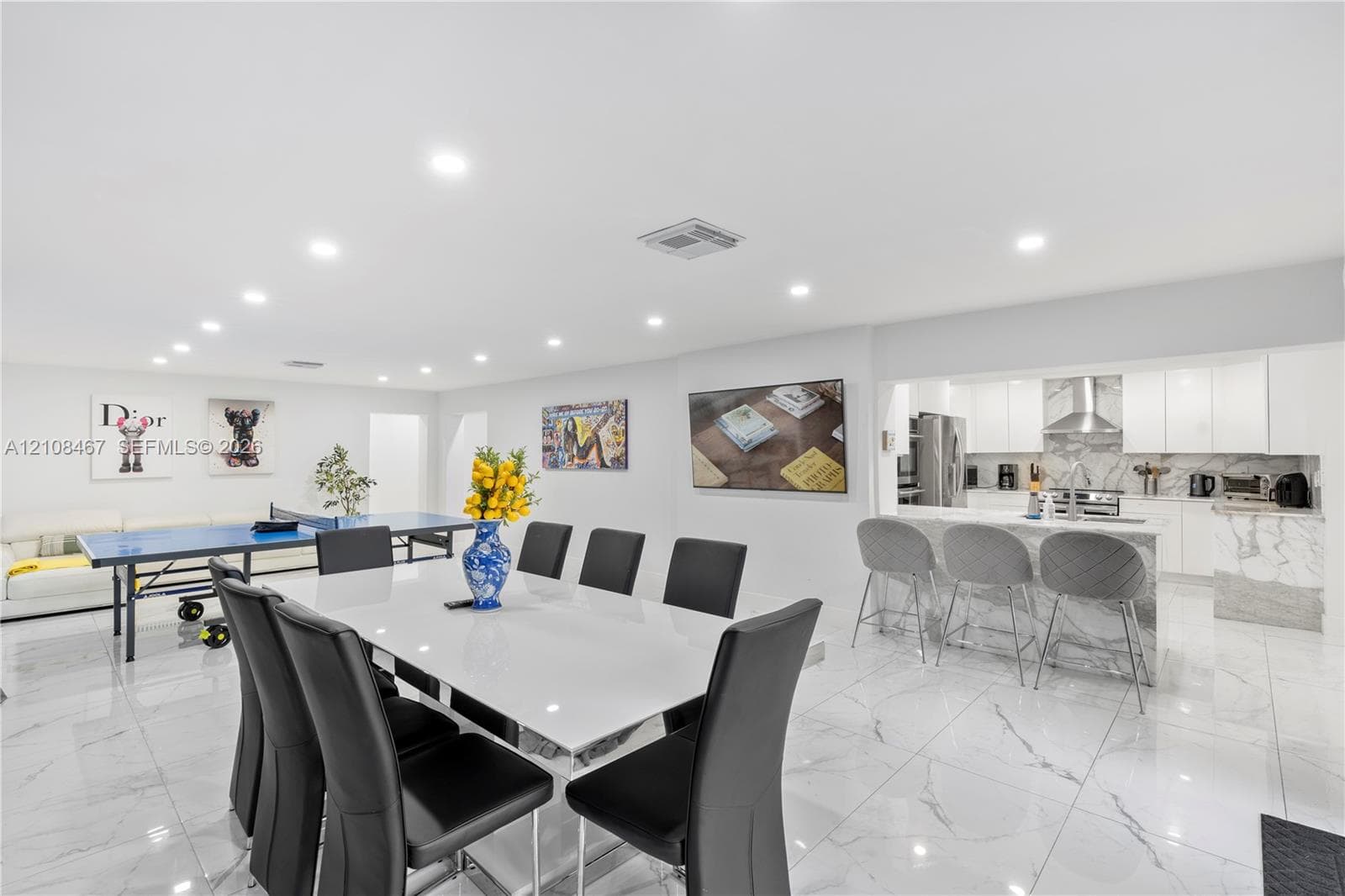 Large-format tile flooring, recessed ceiling lighting, and a kitchen featuring a stone-finish waterfall edge peninsula, white cabinetry, and stainless steel range hood