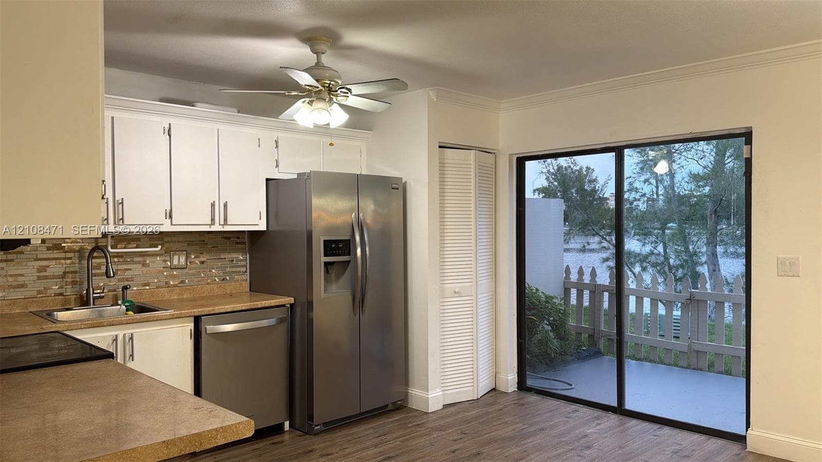 Kitchen featuring white cabinetry, stainless steel appliances, multi-toned stone-tile backsplash, wood-finish flooring, and sliding glass doors with access to an exterior patio