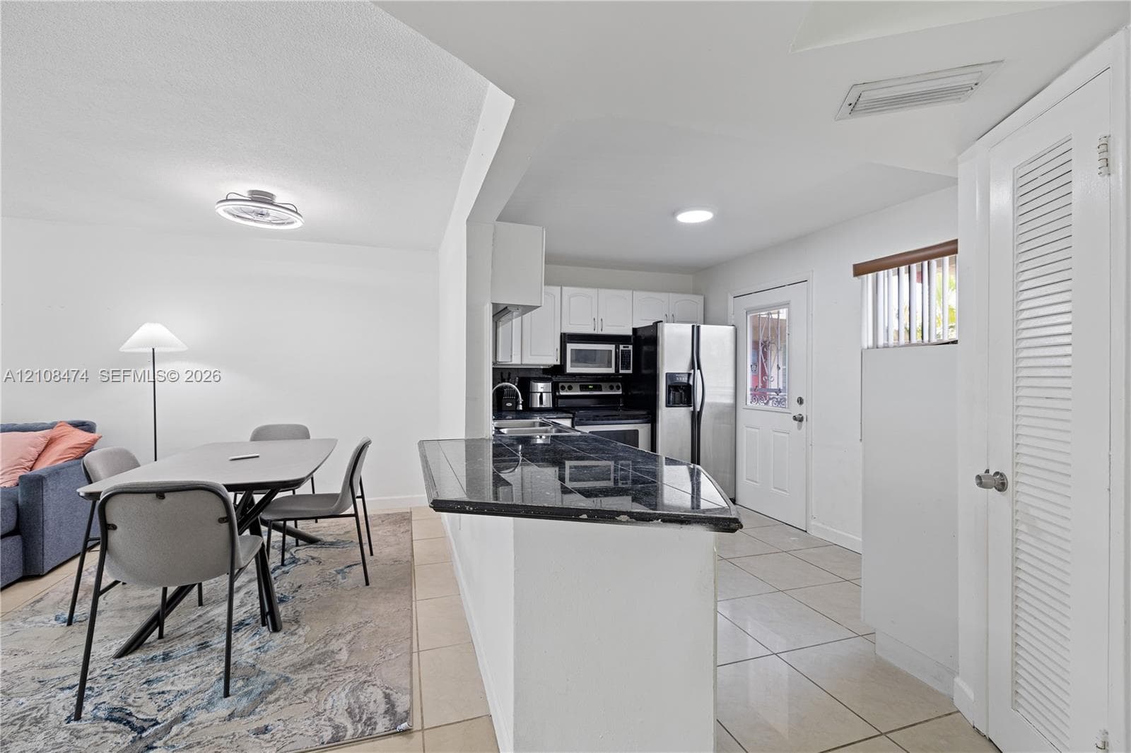 Kitchen featuring dark stone-surfaced breakfast bar, white cabinetry, integrated stainless steel appliances, and neutral tile flooring throughout