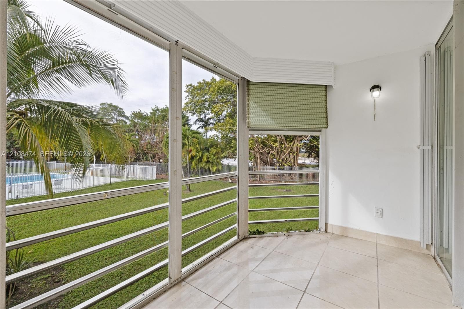 Enclosed patio featuring light-toned tile flooring, floor-to-ceiling screen panels with horizontal railings, and a mounted wall sconce