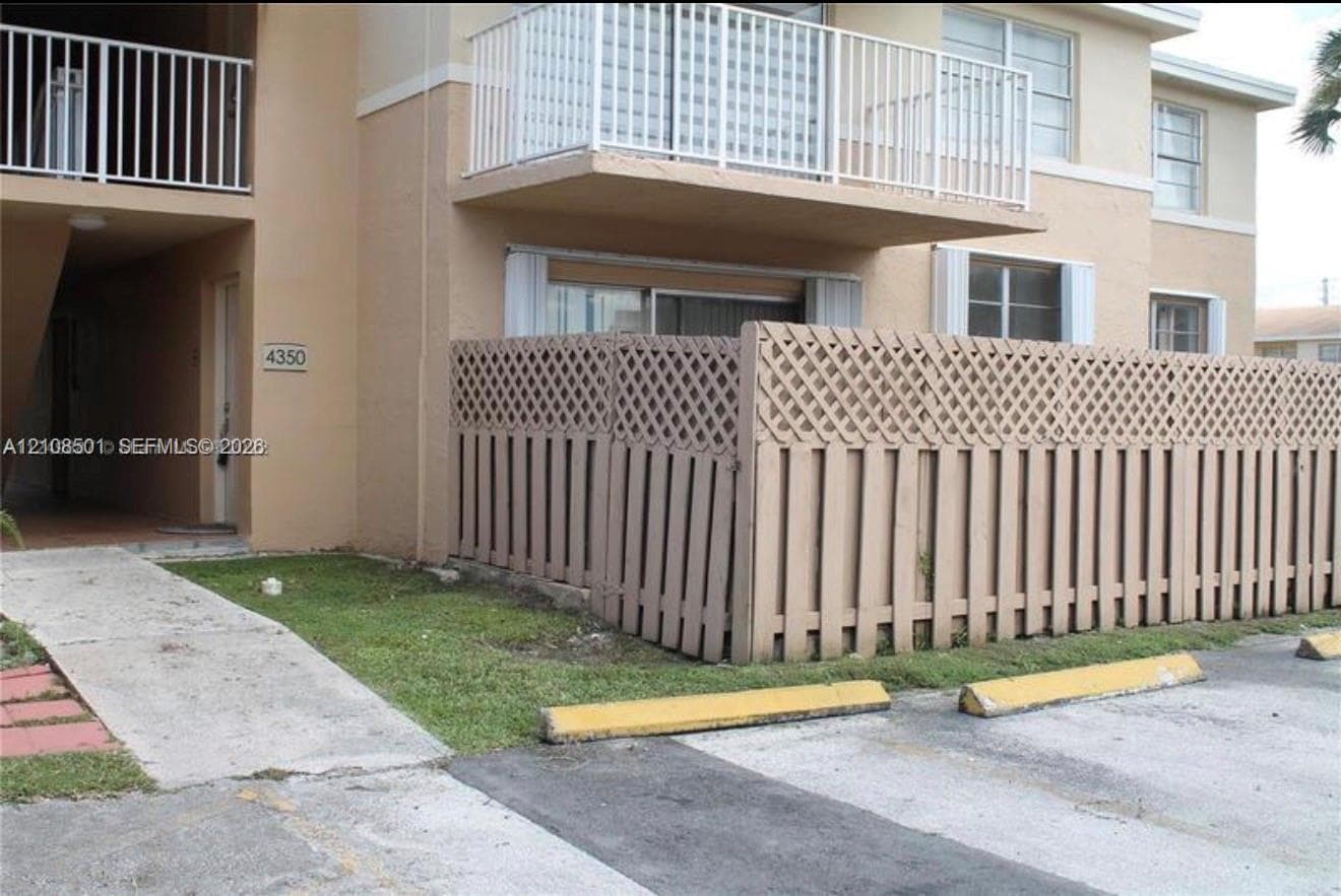 Multi-story stucco exterior featuring a private lattice-top fenced patio, a second-story balcony with white railing, and exterior stairwell access