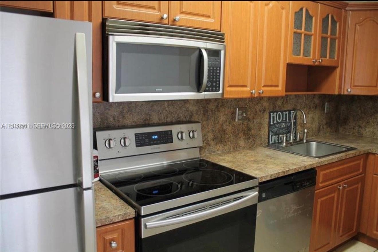 Kitchen featuring stainless steel appliances, wood cabinetry with glass-front accents, laminate countertops, and an integrated microwave