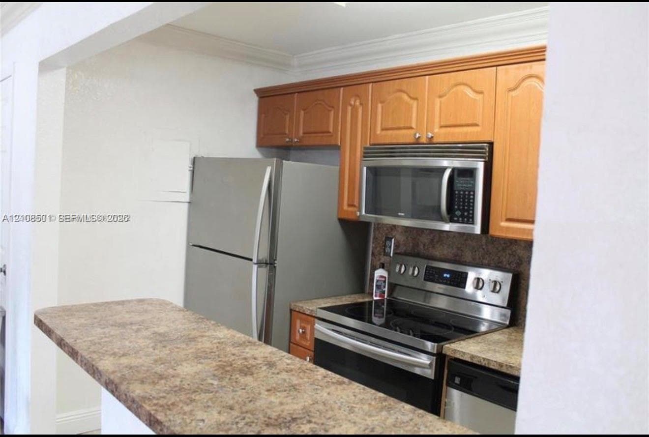 Kitchen featuring wood cabinetry, stone-finish countertops, and stainless steel appliances including a range, microwave, and refrigerator