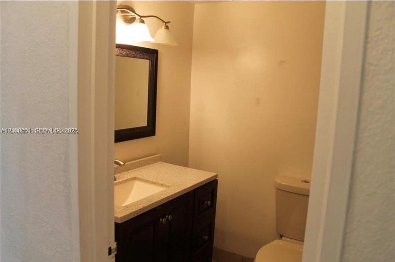 Dark-finish vanity cabinetry with a light-toned stone-surface countertop, integrated white basin, rectangular wall-mounted mirror, and multi-bulb vanity light fixture