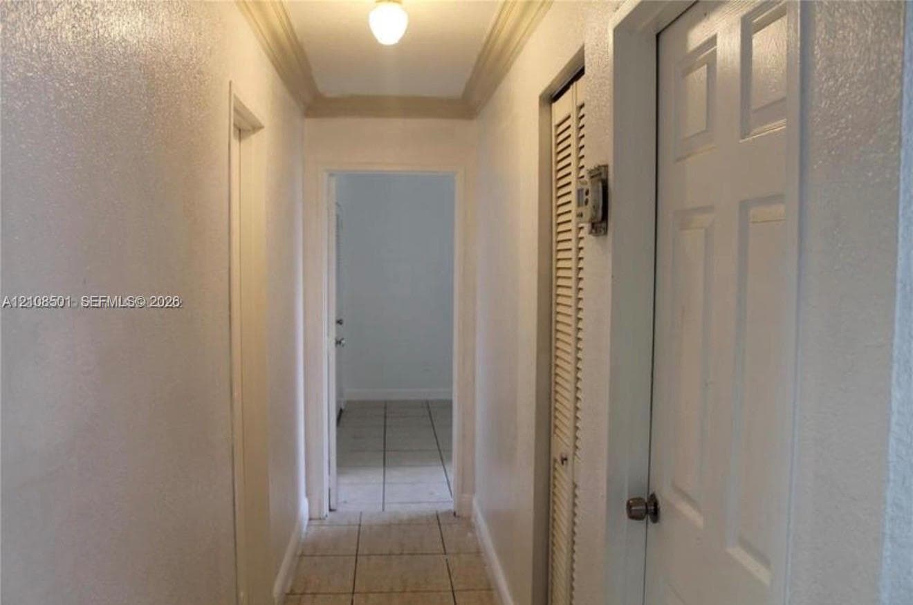 Hallway featuring tiled flooring, crown molding, and louvered closet doors
