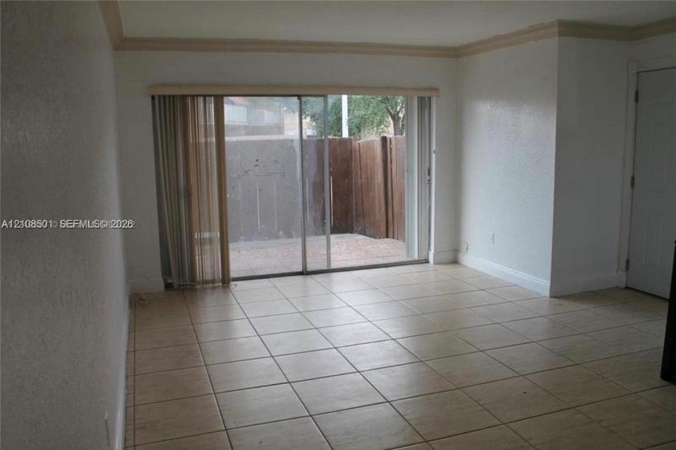 Interior space featuring ceramic tile flooring, crown molding, and sliding glass doors with access to an exterior patio area enclosed by a wood fence