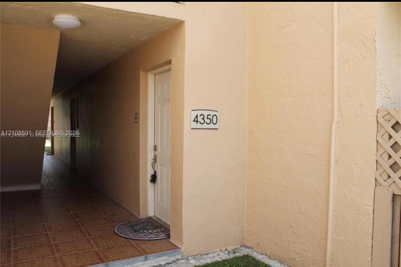 Stucco exterior featuring a covered walkway with ceramic tile flooring and a decorative lattice screen