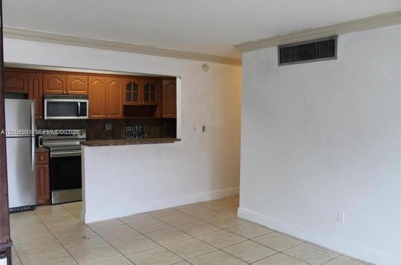 Kitchen featuring wood-finish cabinetry, stainless steel appliances, pass-through counter, and ceramic tile flooring