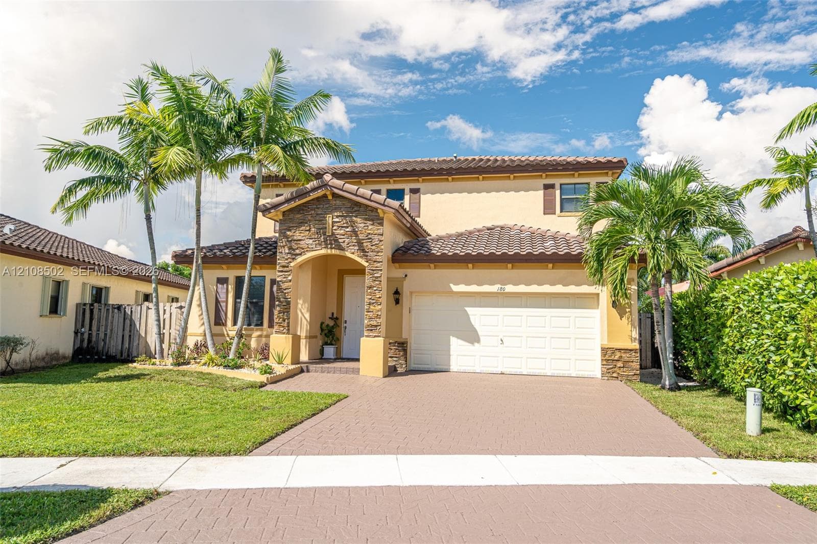 Two-story exterior featuring a stone-veneer entryway, tile roof, stucco facade, paved driveway, and mature landscaping