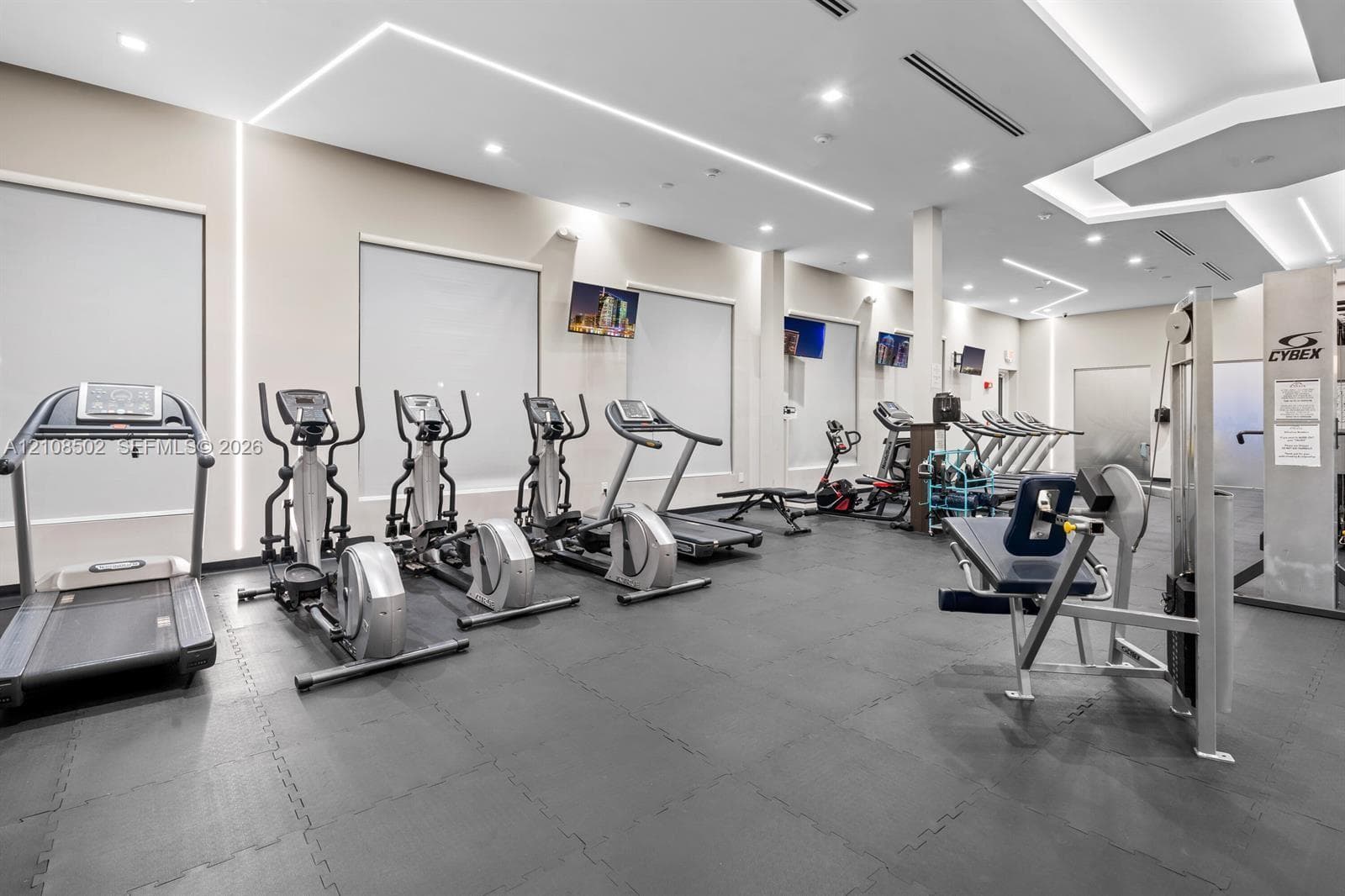 Fitness area featuring recessed ceiling lighting, linear wall-mounted accent illumination, neutral wall finishes, and rubberized flooring